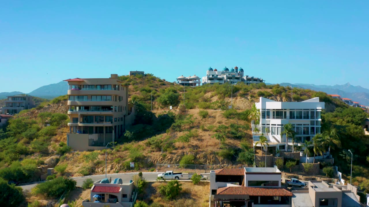 Residential buildings on a dry green hillside with roads and parked cars.
