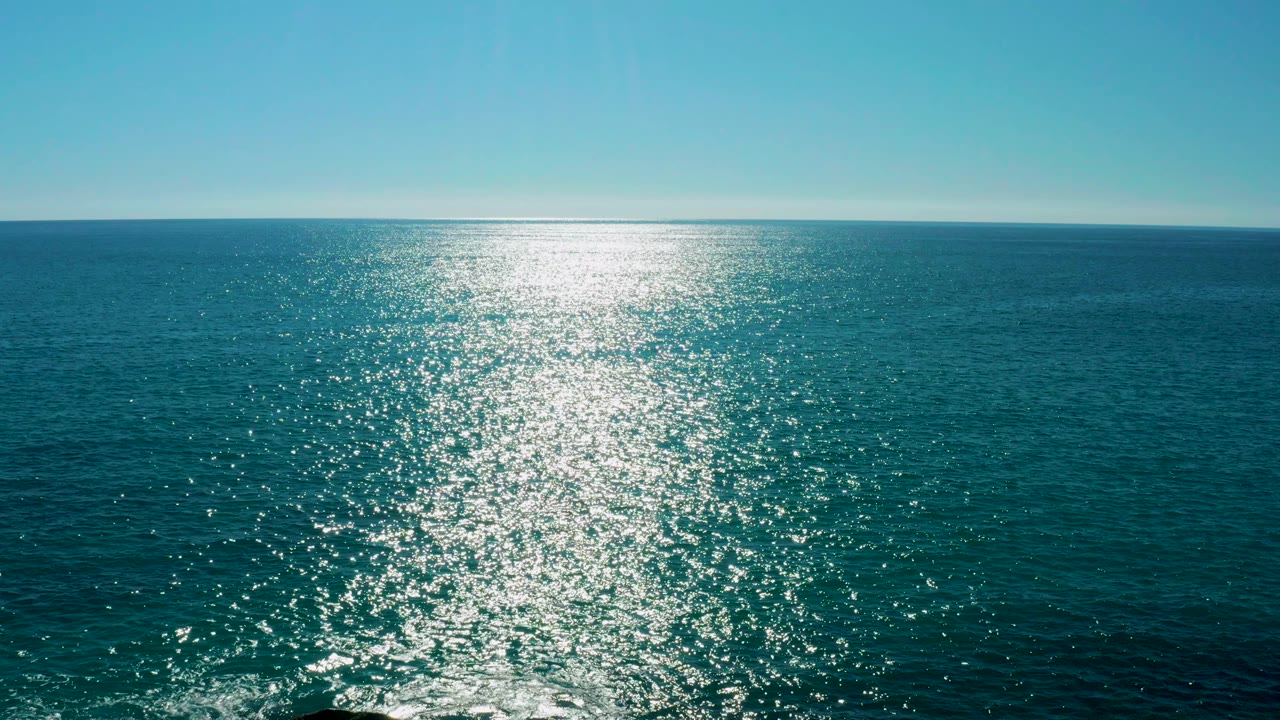Wide view of the ocean off San Jose del Cabo with a bright sun reflection near the left side of the water path and no visible people.