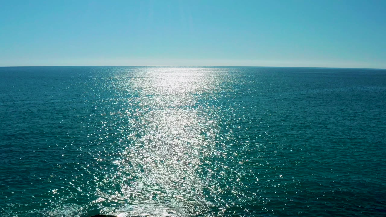 Open ocean near San Jose del Cabo with the sun glint centered more strongly across the rippled surface and no visible people.