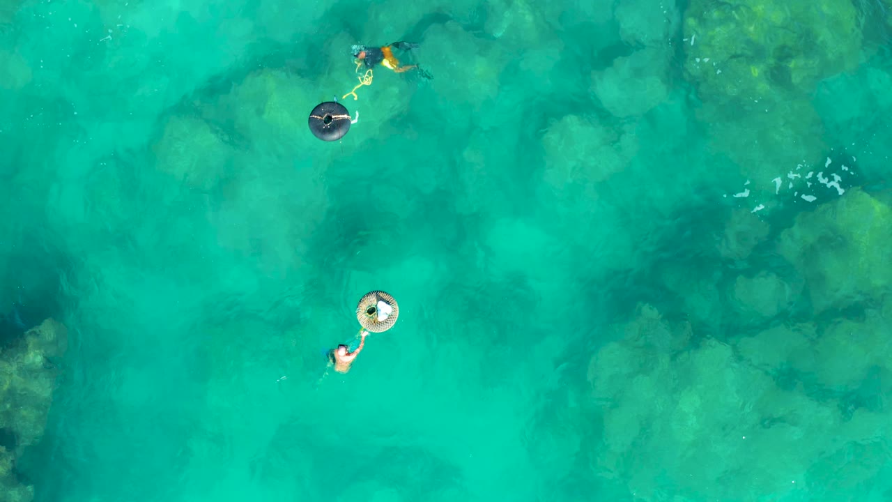 Two swimmers and inflatable rings over shallow turquoise water.