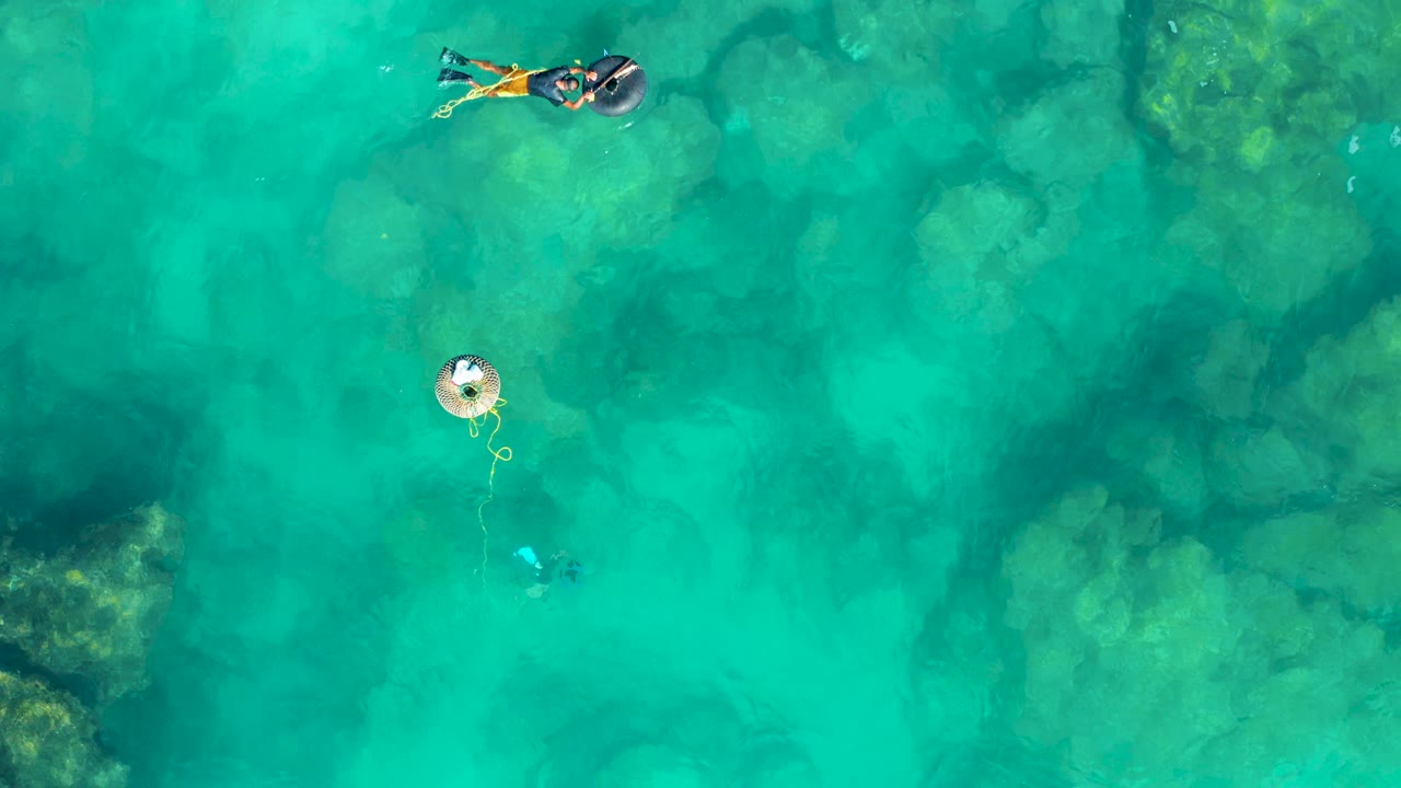 Swimmer and float viewed from above in clear green-blue water.