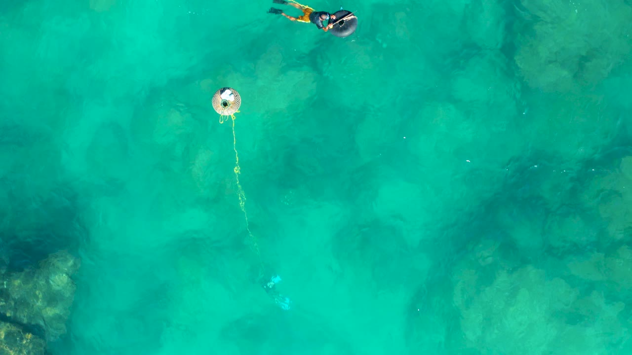 Overhead San Jose del Cabo frame with the snorkeler more fully inside the shot near the top, a buoy lower left, and rope visible between them over clear green-blue water.