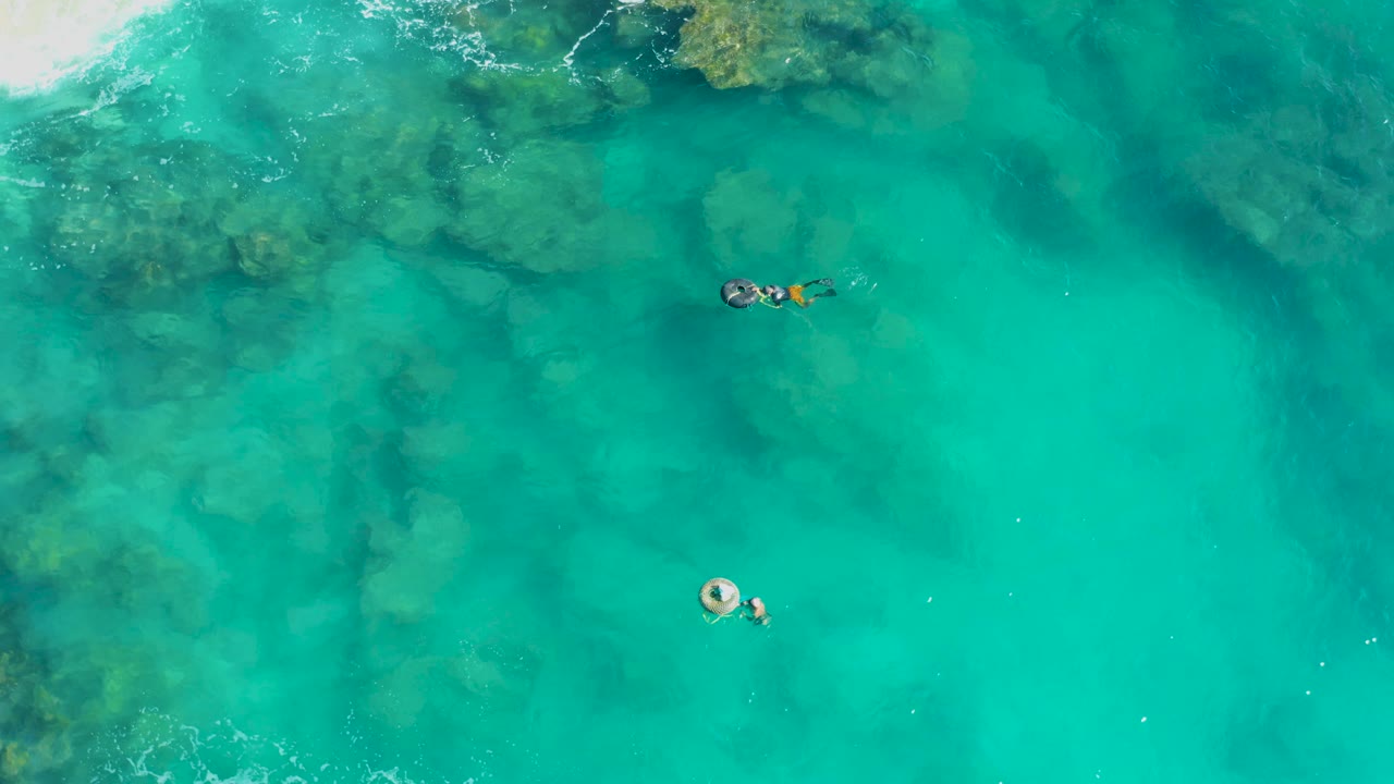 Top-down San Jose Del Cabo water view with a swimmer near a round float and another small group higher in frame beside mottled reef color.