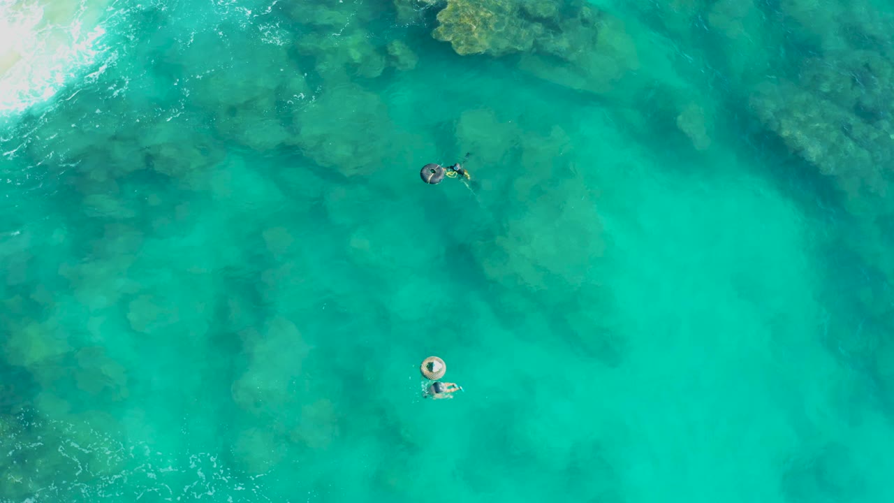 Two people floating in clear water with underwater rocks visible