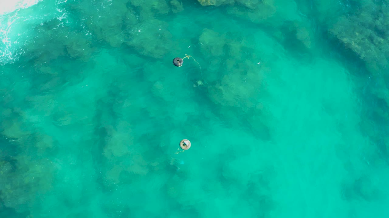 Overhead turquoise water with two small floating buoys