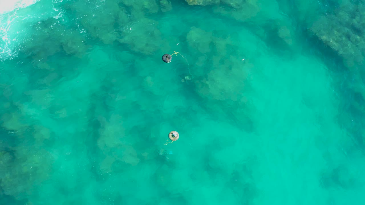 Clear blue-green water in San Jose Del Cabo shows a pale lower buoy, a darker upper buoy, underwater shapes, and no visible people.