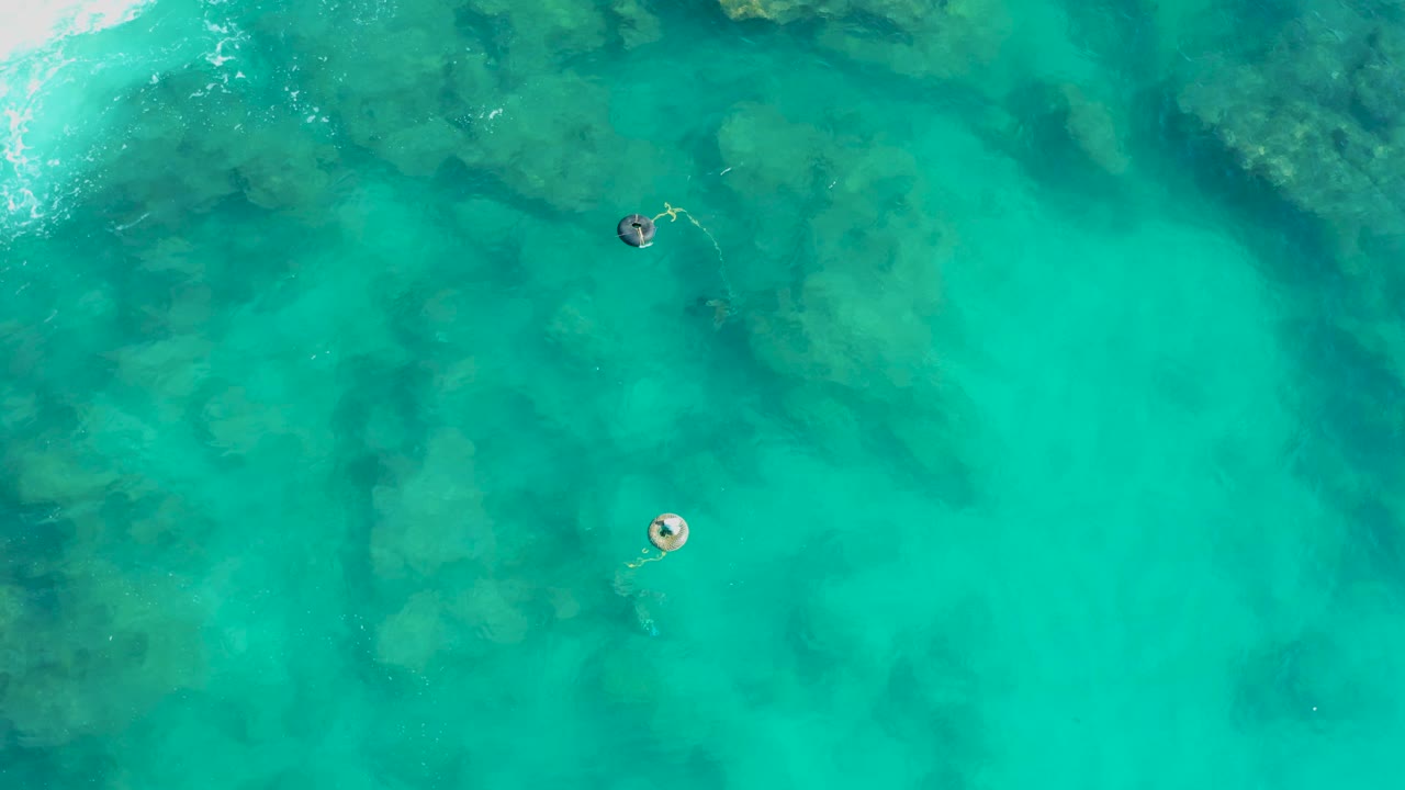 Turquoise ocean water in San Jose Del Cabo fills the frame with two small buoys, darker submerged patches, and no visible people.