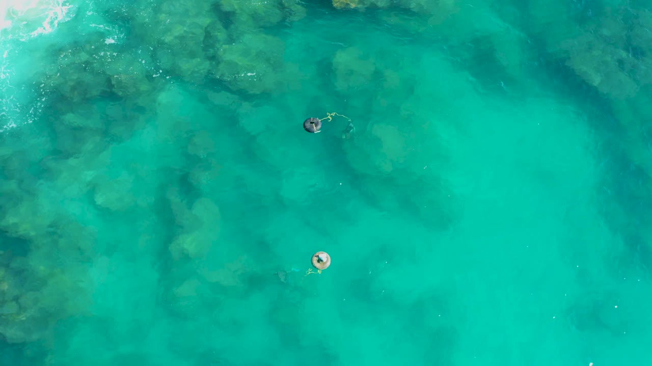 Two people in clear turquoise water, one floating and one swimming nearby.