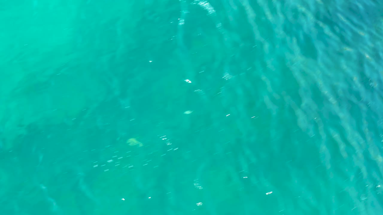Green-blue water in San Jose Del Cabo reveals uneven submerged rocks and light patterns under the surface, with no visible people.