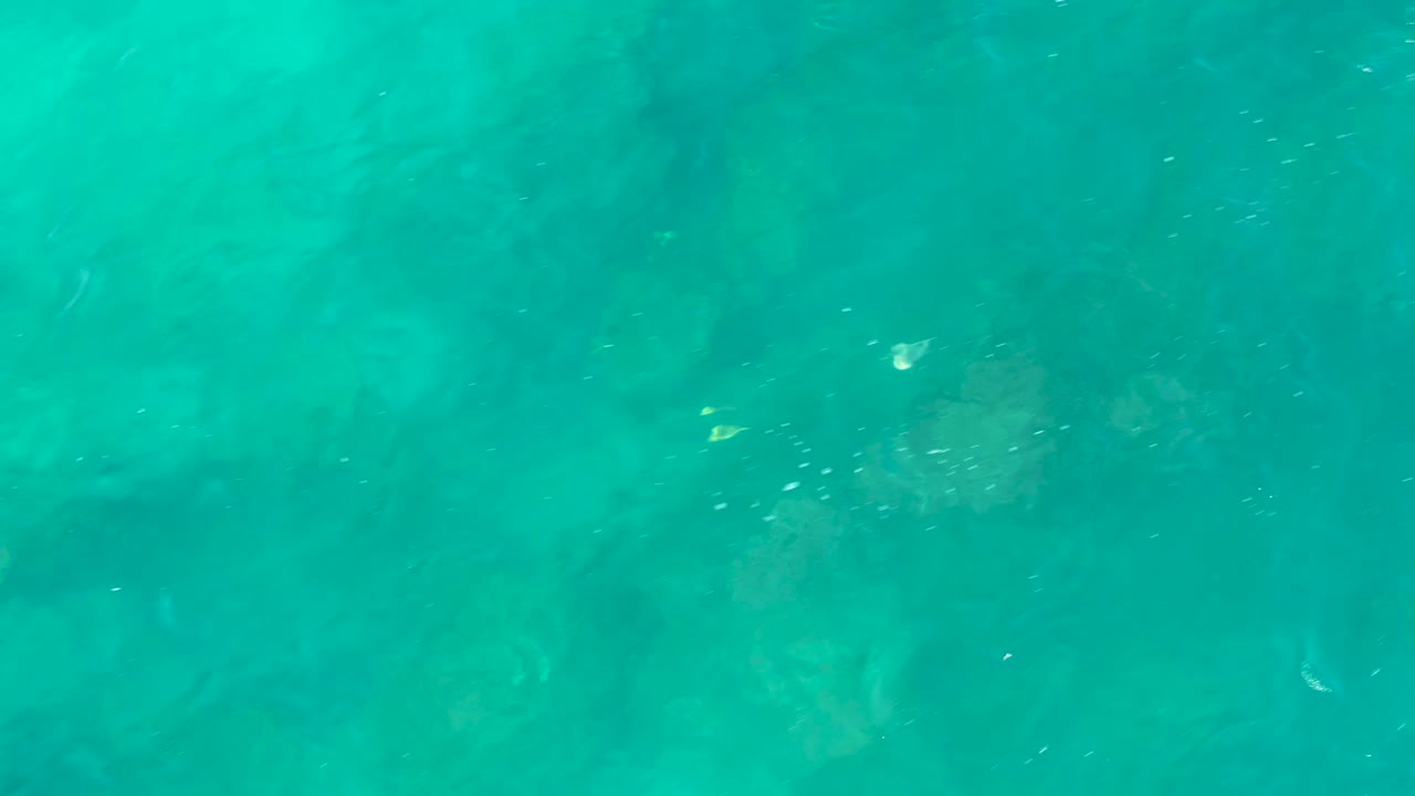Turquoise water in San Jose Del Cabo fills the frame with rippled surface texture and faint rocks visible below, with no visible people.