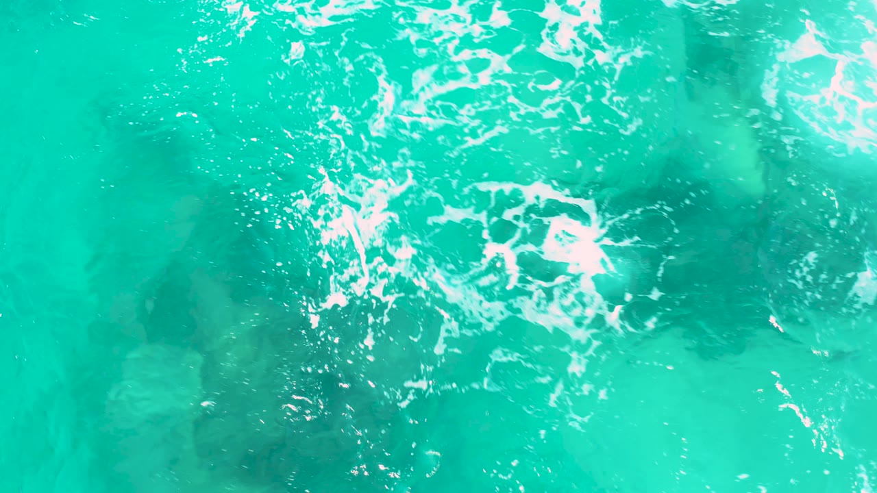Top-down San Jose Del Cabo water frame with blue-green clarity, scattered white foam at the top, pale seabed areas, and no visible people.
