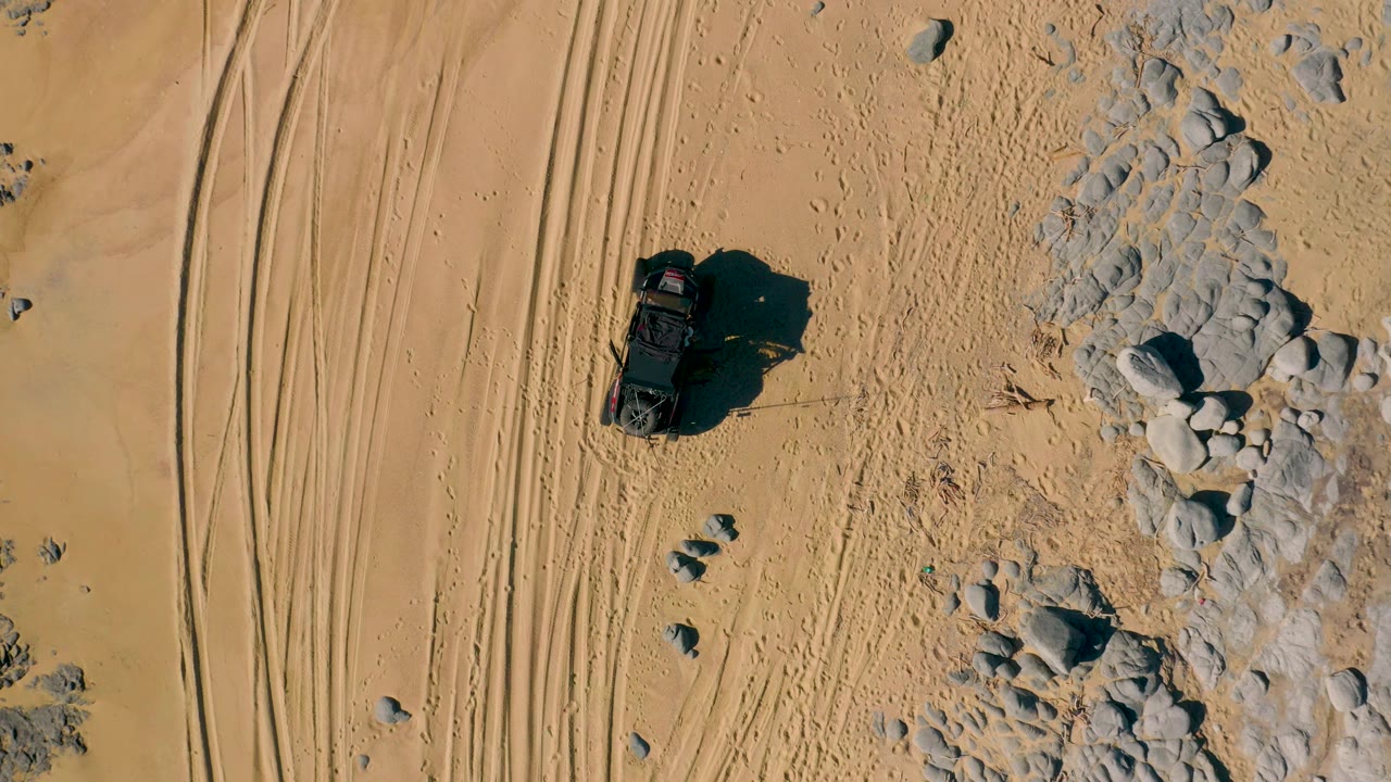Top-down desert SUV beside tracks and pale rock outcrop