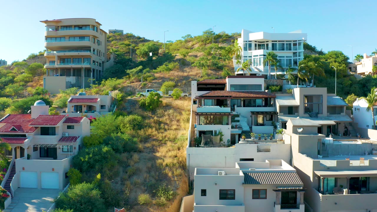 Residential hillside with modern houses, shrubs, and a small road.