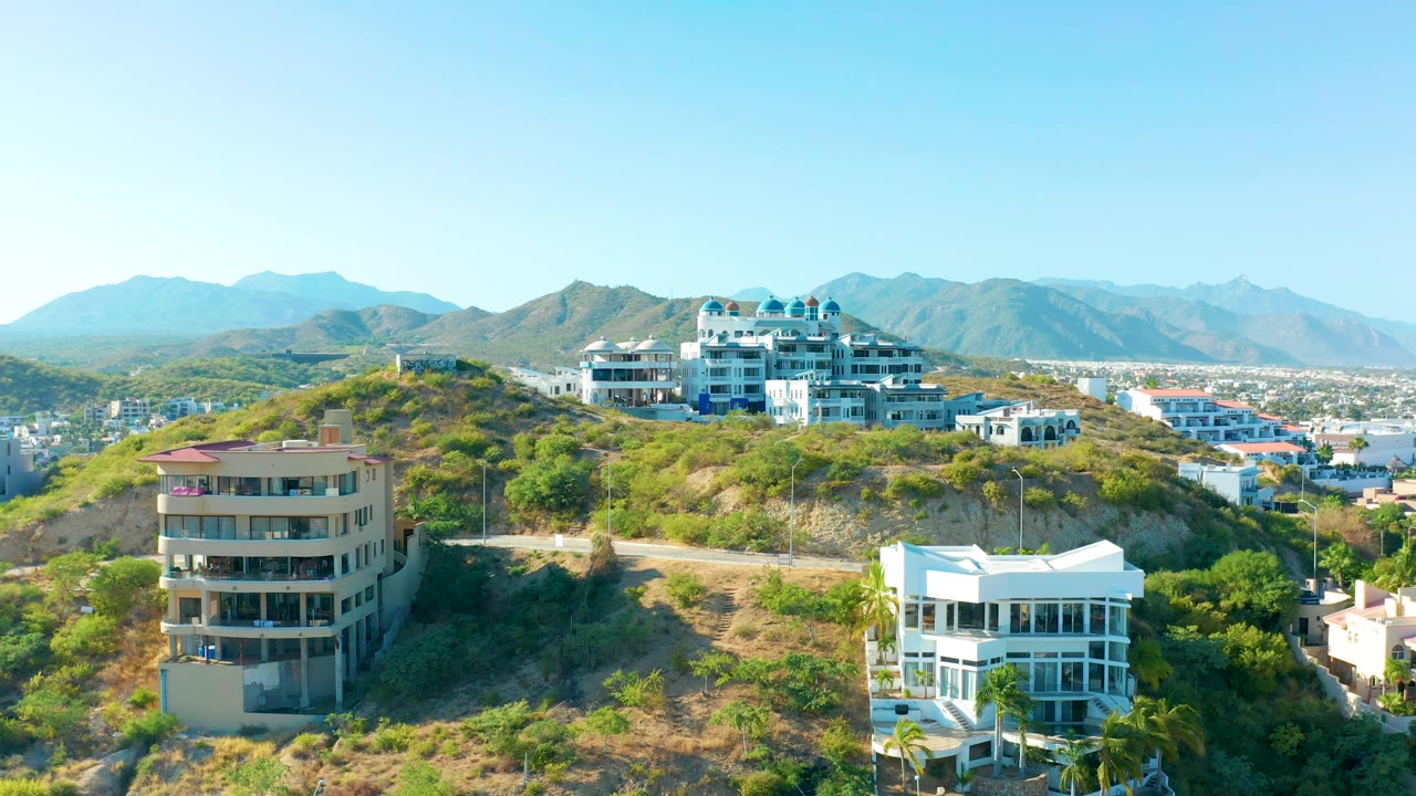 Residential hillside with white and beige buildings below distant mountains.