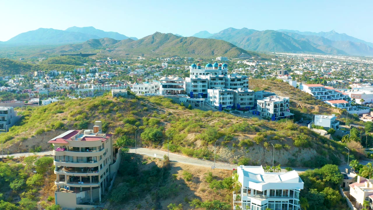Hillside residential buildings with road and mountains beyond.