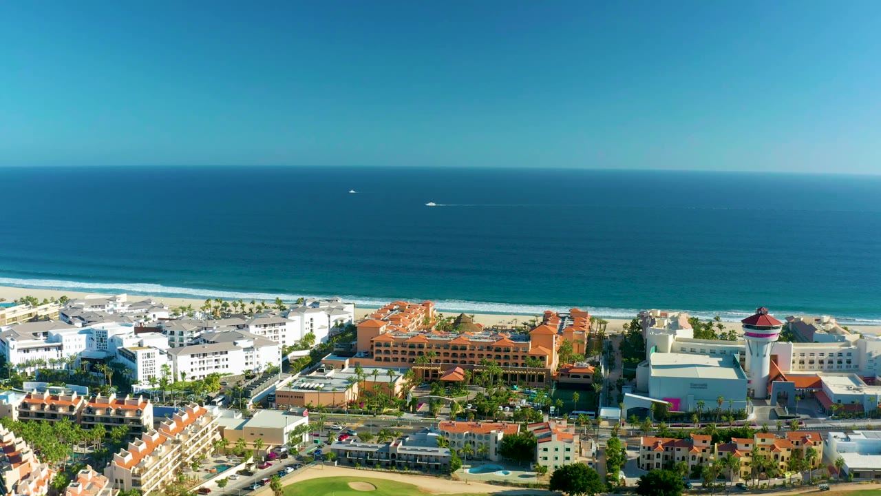 San Jose del Cabo aerial view with the beach and ocean spanning the upper frame, clustered white buildings in the foreground, orange roofs near center, and no visible people.