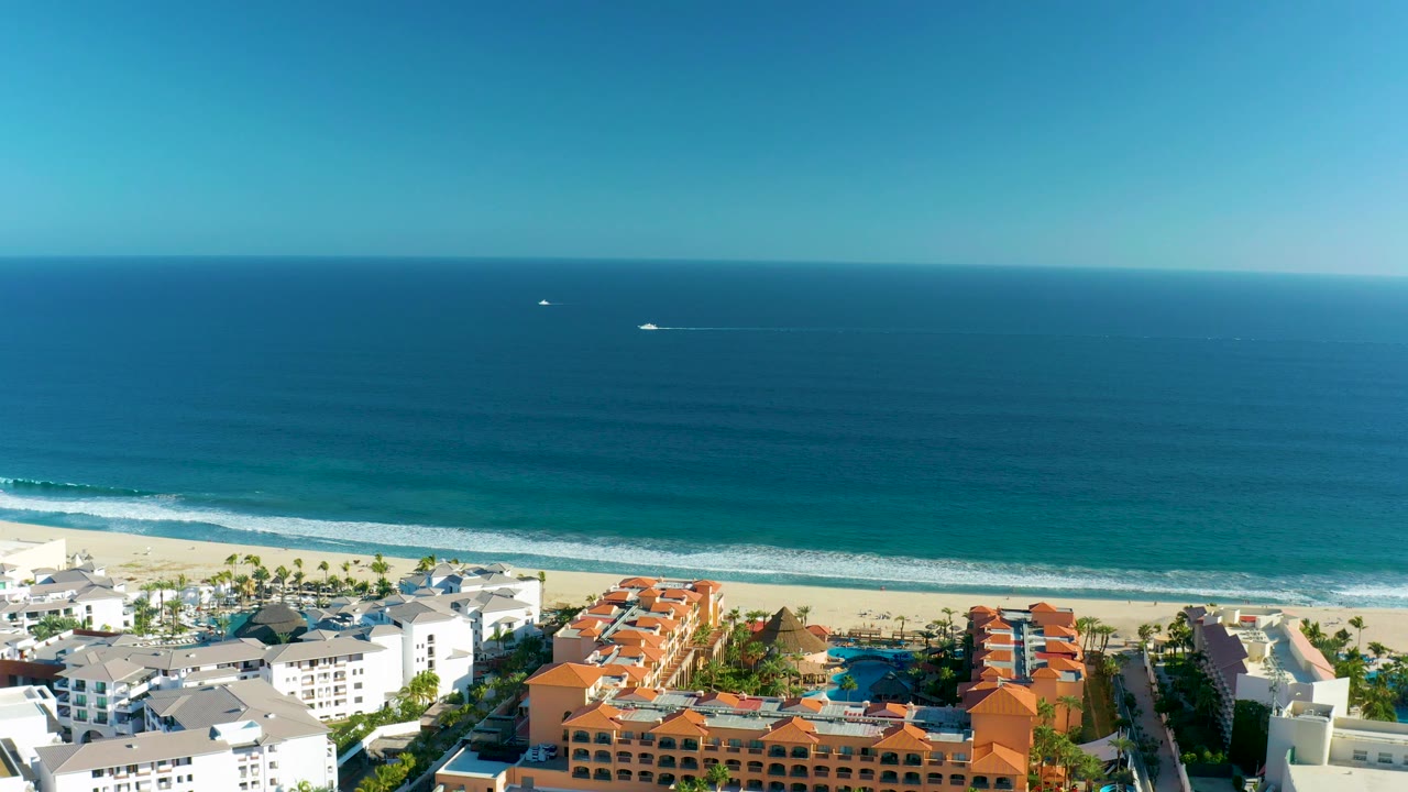 Aerial coastline with beachfront buildings and calm ocean water.