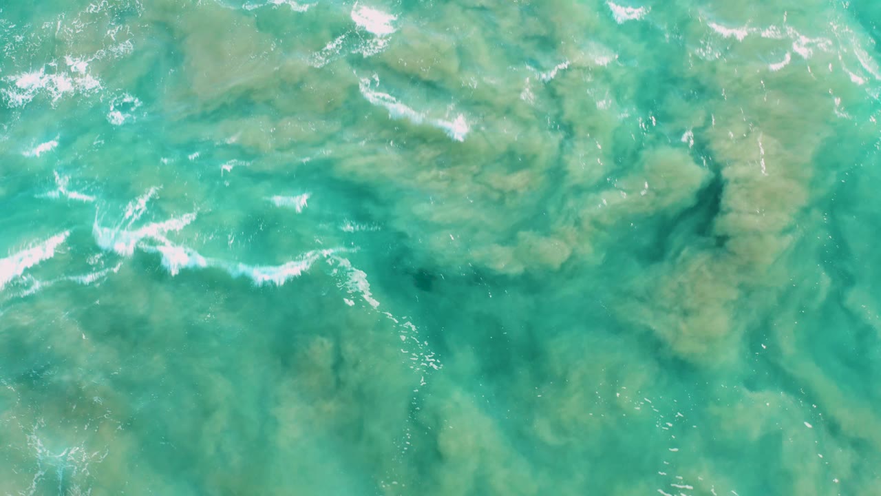 Overhead San Jose del Cabo water frame with tan-green algae or sediment forms, bright turquoise current lines, white foam, and no visible people.