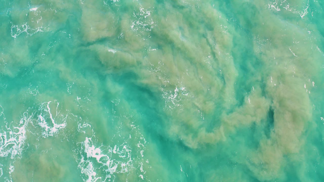 Overhead turquoise ocean water with algae and small foam lines.
