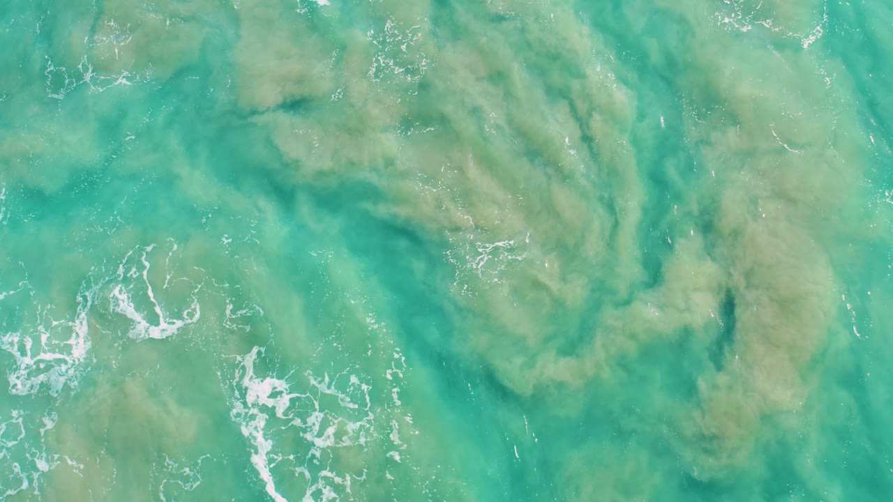 Overhead San Jose Del Cabo water view with diffuse greenish-brown sediment patterns, pale highlights on the turquoise surface, and no visible people.