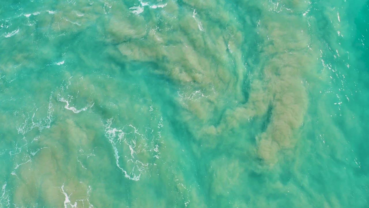 Overhead turquoise ocean water with sandy seabed patterns.