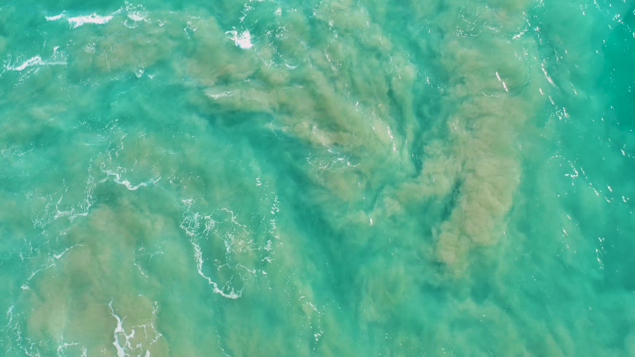 Turquoise shallow sea in San Jose del Cabo shows darker sand contours beneath rippled water, with thin white surface lines and no visible people.