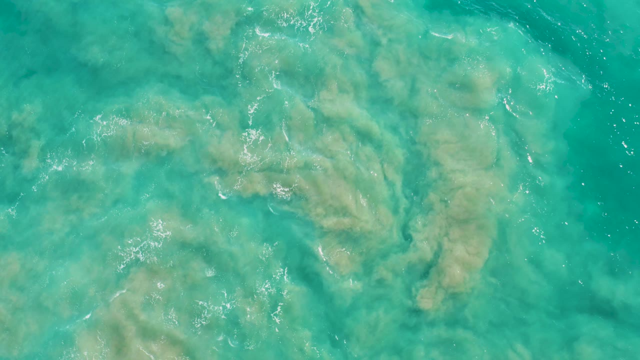 Clear turquoise ocean water in San Jose Del Cabo shows a broad pale sand patch shifting under the surface, with no visible people or shoreline.