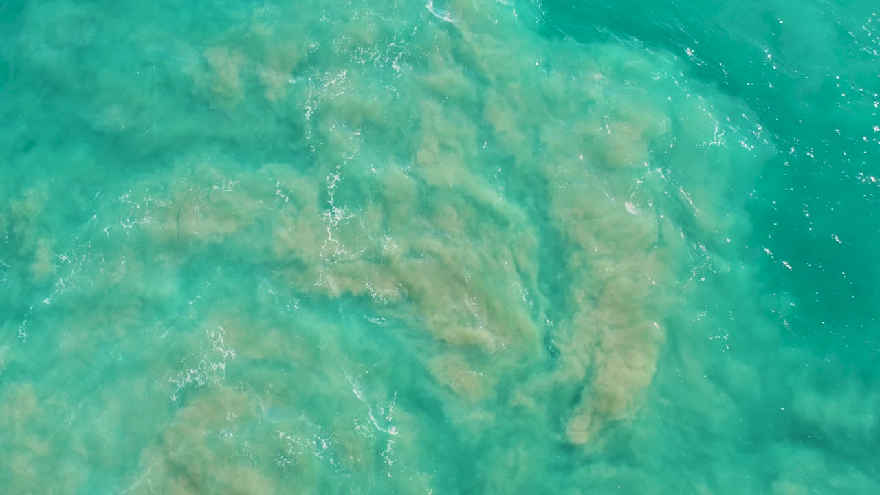 Overhead turquoise water in San Jose Del Cabo reveals soft pale sand shapes beneath the surface, with subtle wave lines and no visible people.
