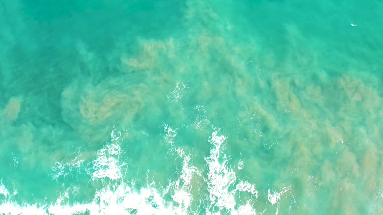 Aerial frame of clear turquoise water over sandy seabed in San Jose Del Cabo, with broken white foam near the bottom and no visible people.