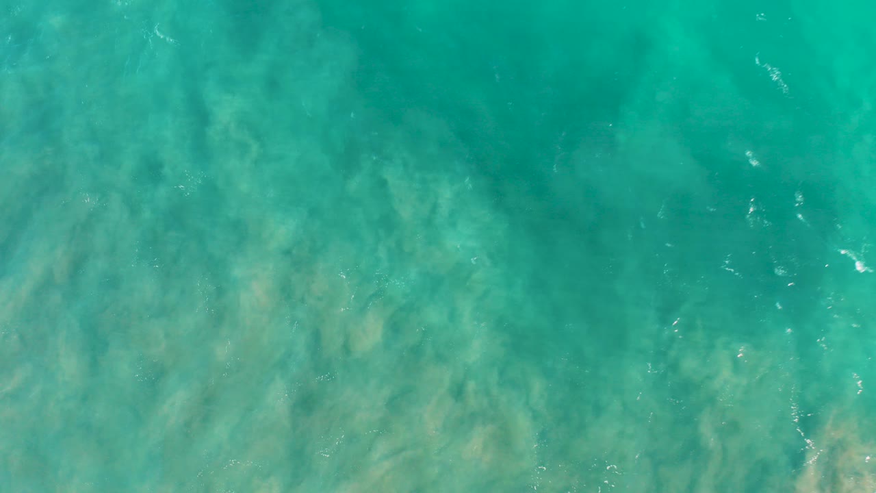 Overhead view of clear turquoise ocean water in San Jose del Cabo with sandy seabed visible beneath soft ripples and no visible people.