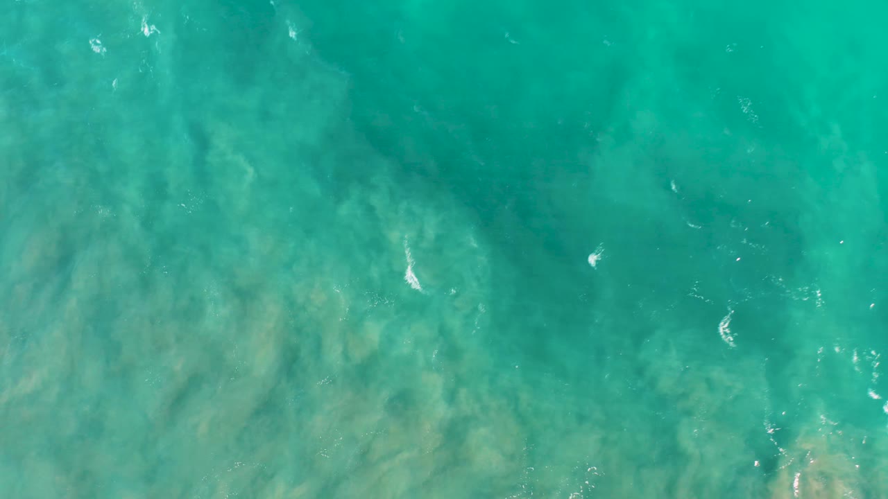 Shallow turquoise sea in San Jose del Cabo fills the frame, with cloudy beige seabed marks visible through the water and no visible people.