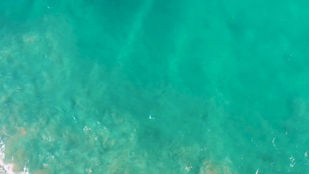 Turquoise water in San Jose del Cabo fills the frame, with darker wave bands crossing the surface and the seabed faintly visible, with no visible people.