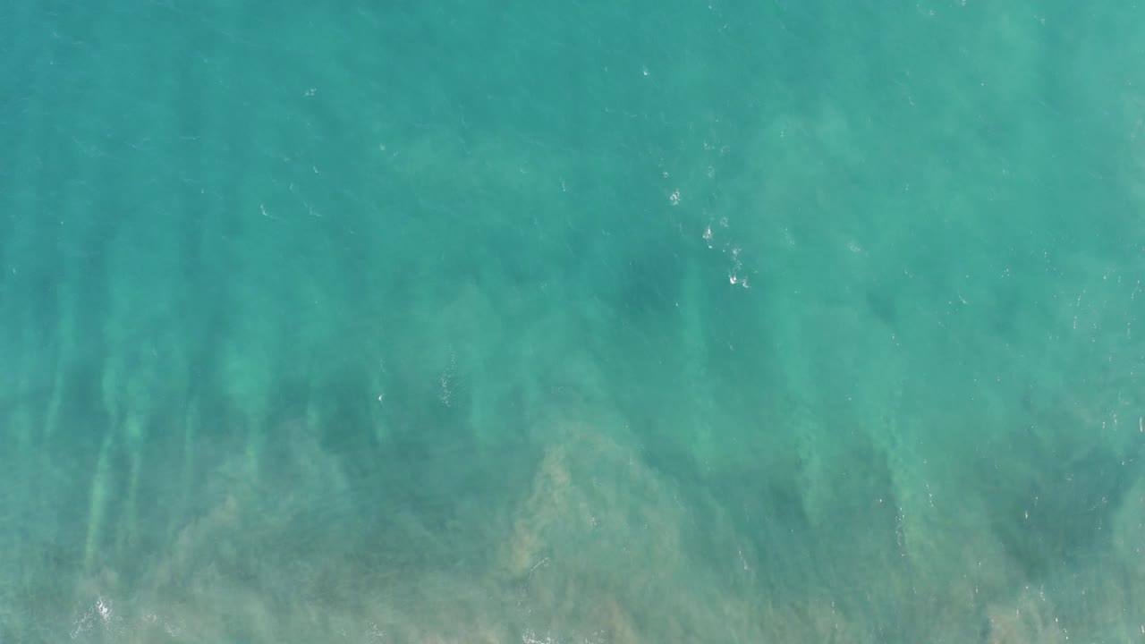 Overhead view of clear turquoise water in San Jose Del Cabo with a pale rocky seabed and faint surface ripples, no visible people.