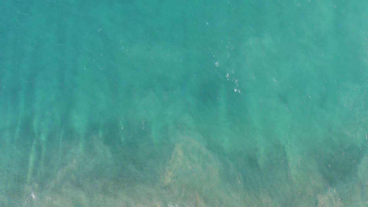 Clear blue-green water in San Jose Del Cabo shows darker submerged streaks and soft ripple patterns across the surface, no visible people.
