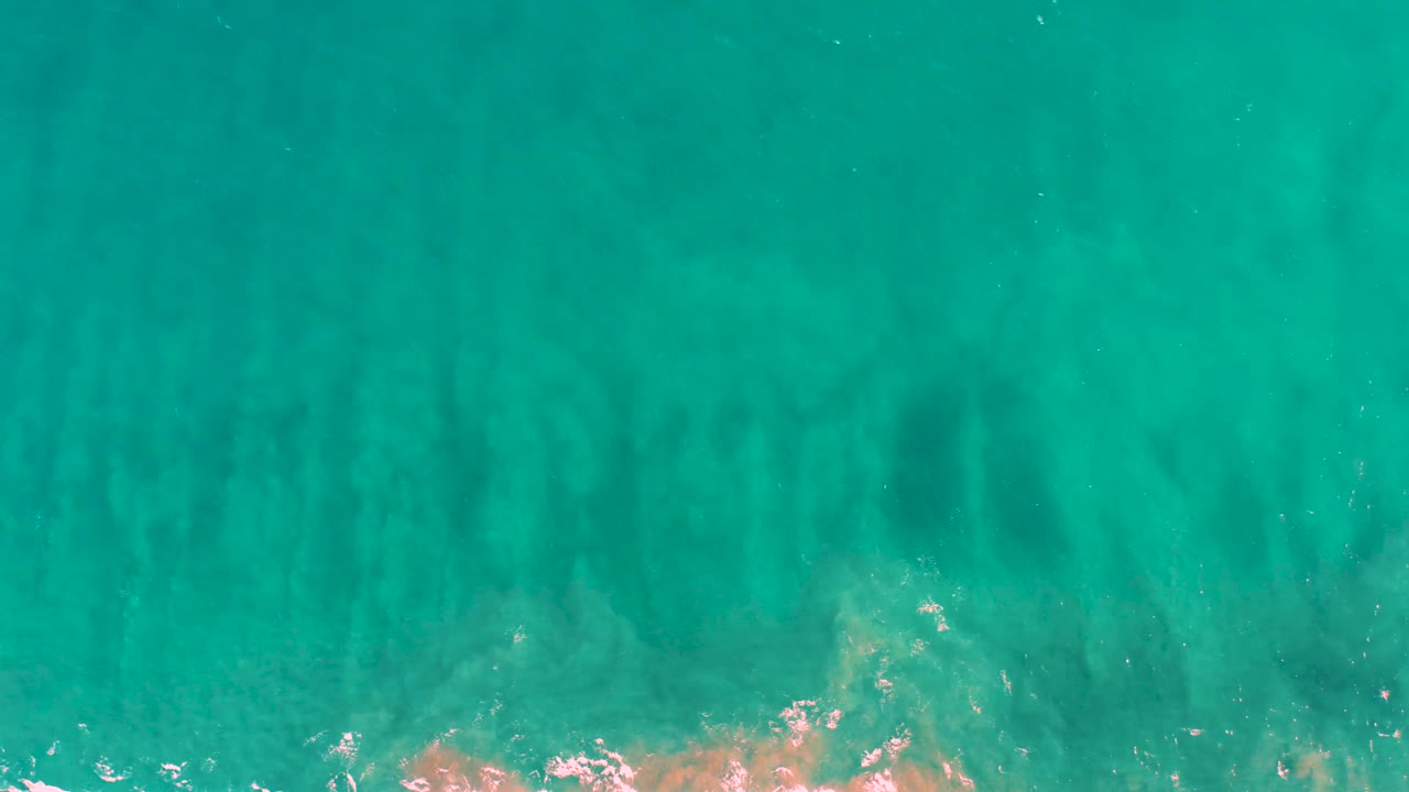 Top-down San Jose Del Cabo shoreline water with milky sand formations below the surface, brighter foam along the lower border, and no visible people.