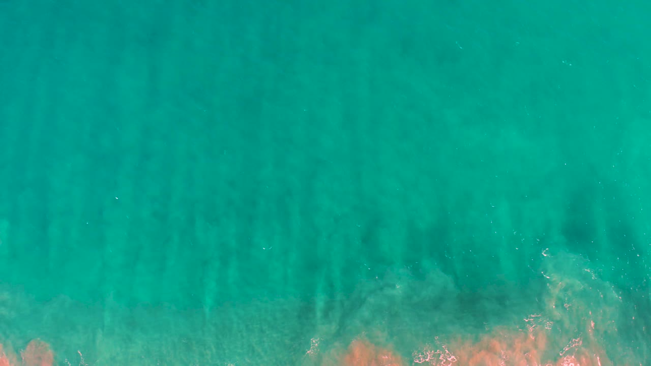 Turquoise shallow sea with a larger pale underwater patch and dark streaks across the frame.