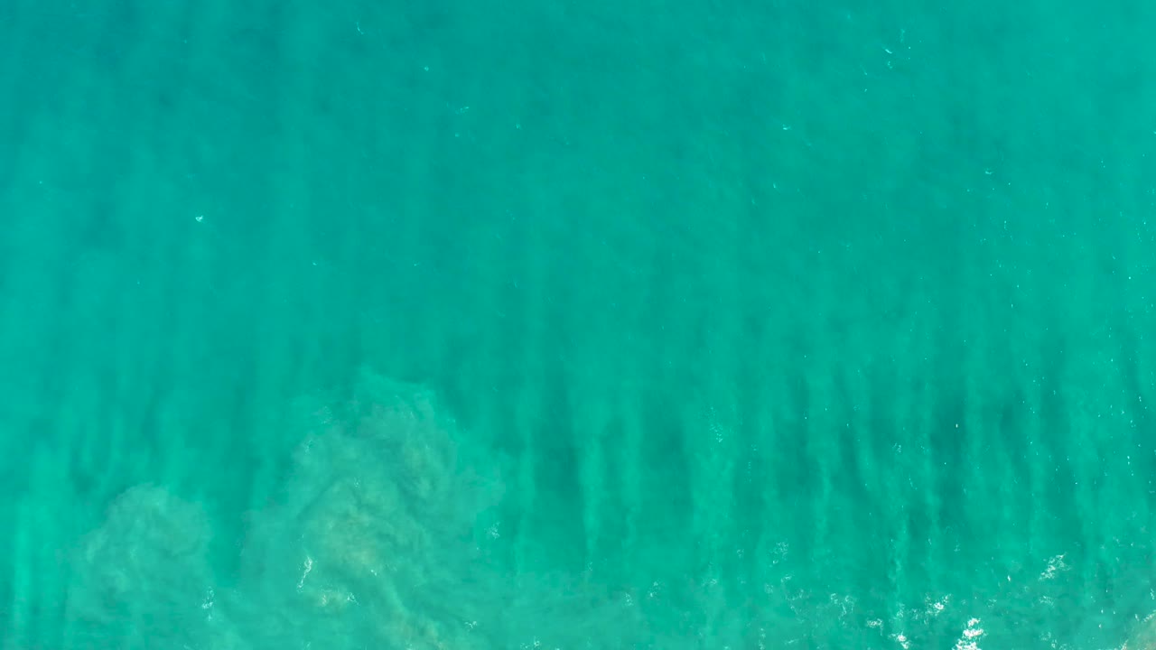 Clear San Jose del Cabo ocean water fills the frame with darker vertical underwater bands, faint white foam flecks, and no visible people.