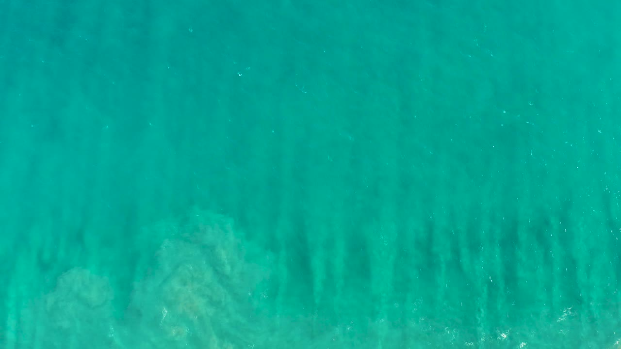 Aerial turquoise water with faint submerged vegetation and soft surface texture.