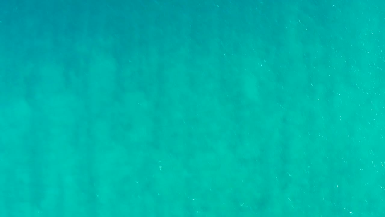 Blue green underwater frame from San Jose Del Cabo, Baja California Sur, with drifting white specks over the sandy ocean floor and no visible people.