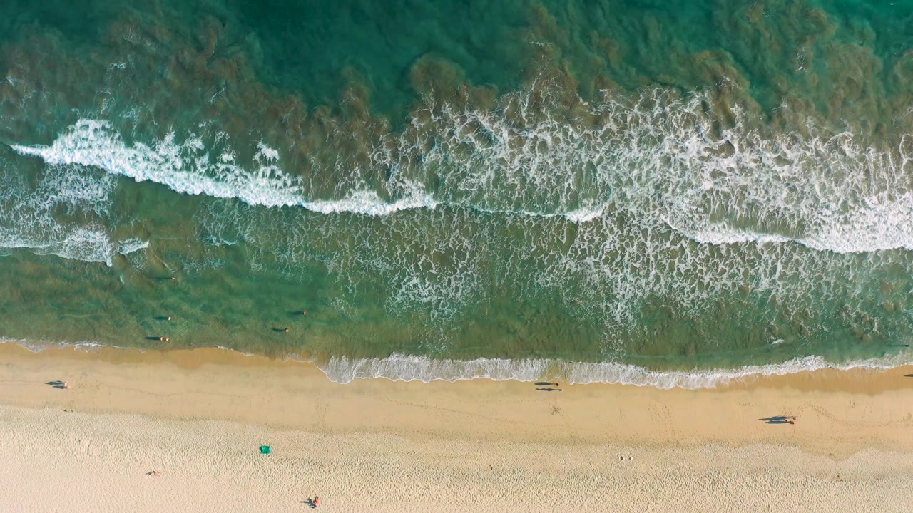 White foam spreads across shallow green water beside sand.