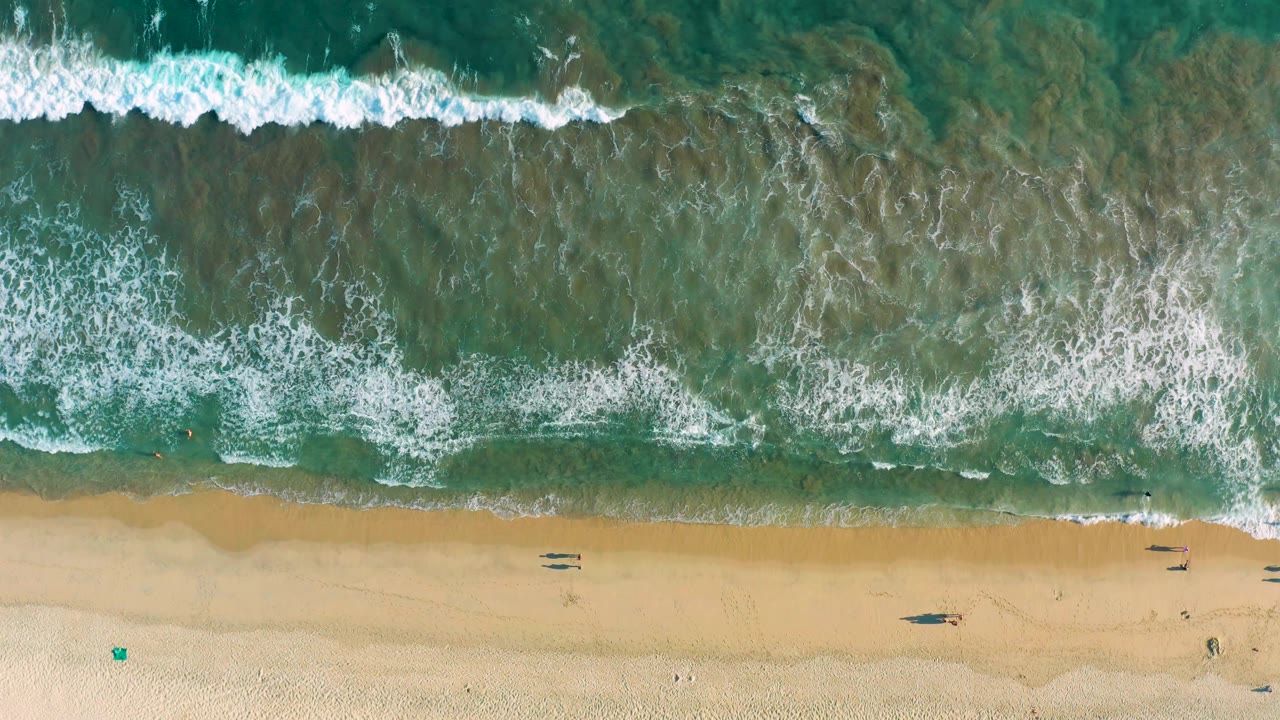 Overhead beach frame from San Jose del Cabo with whitecaps across shallow turquoise water and a smooth sandy strip below.