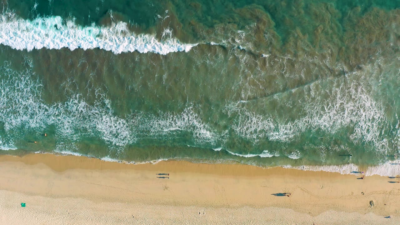 Wide overhead view of waves crossing a sandy shoreline.