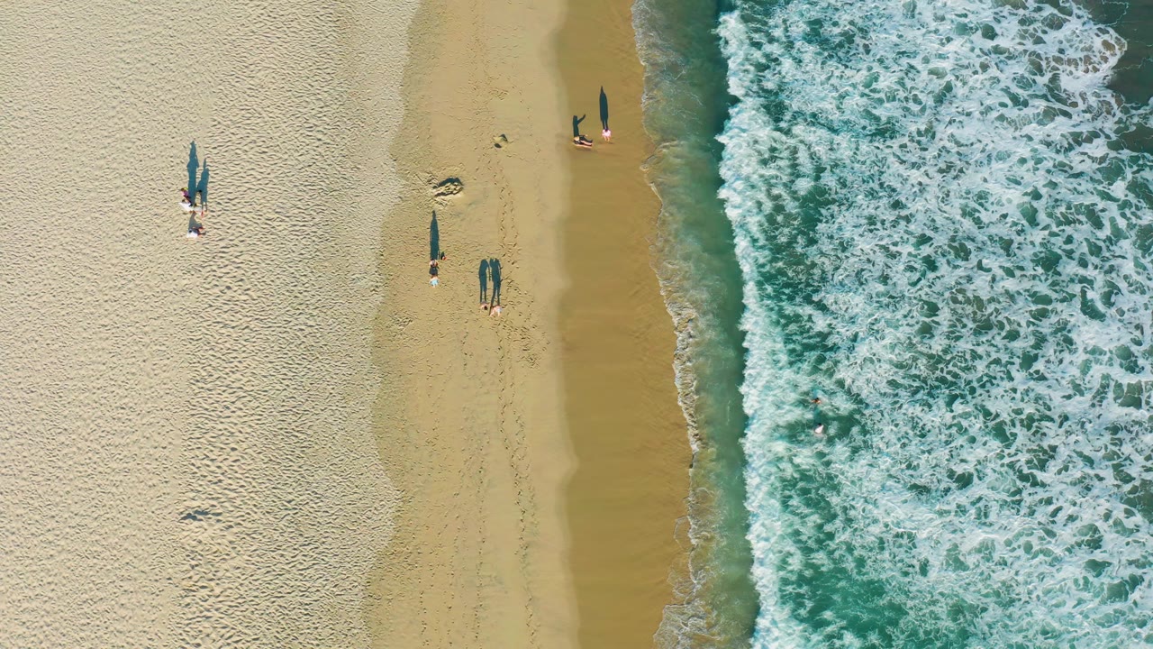 Aerial shoreline view with people standing near the surf.