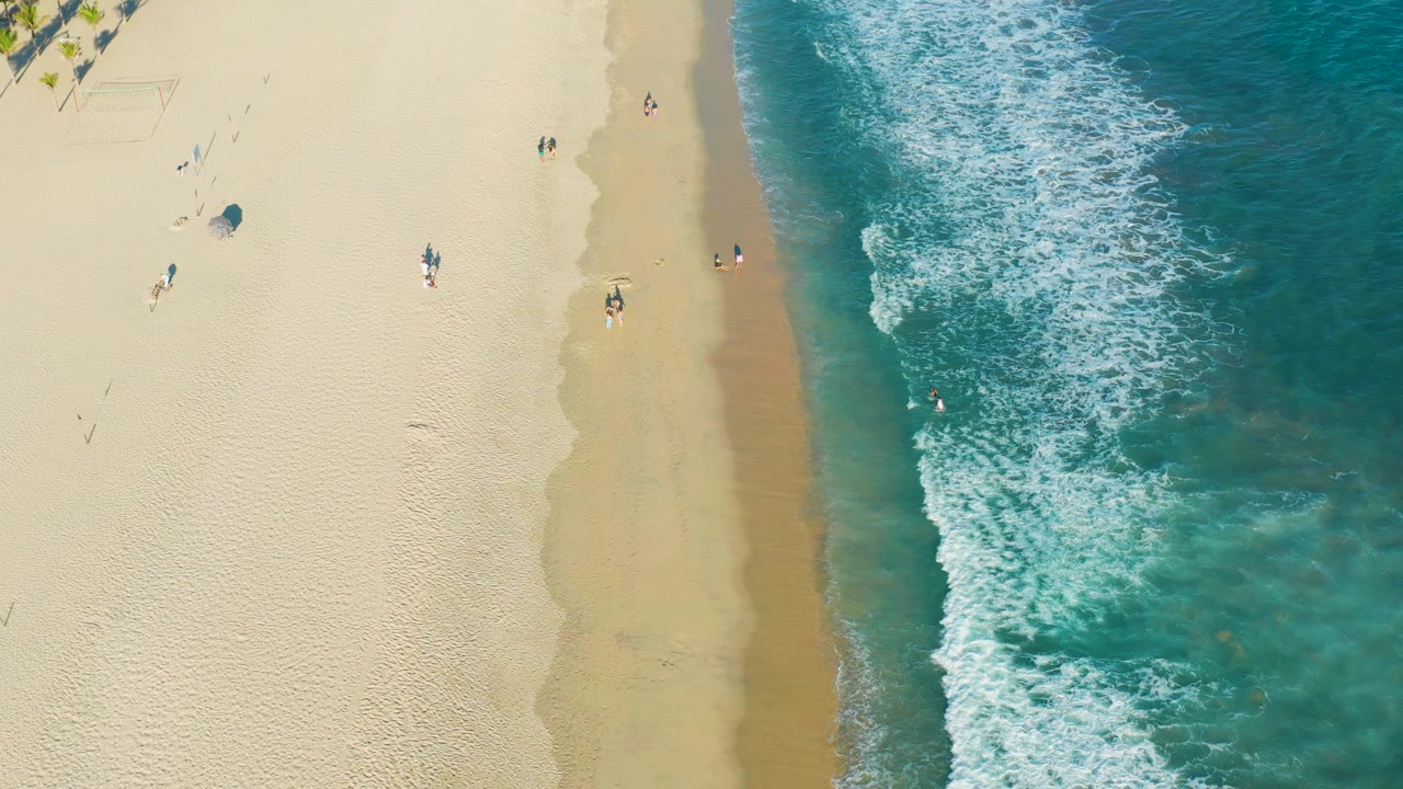 Aerial shoreline with breaking waves and people on sand and in water.