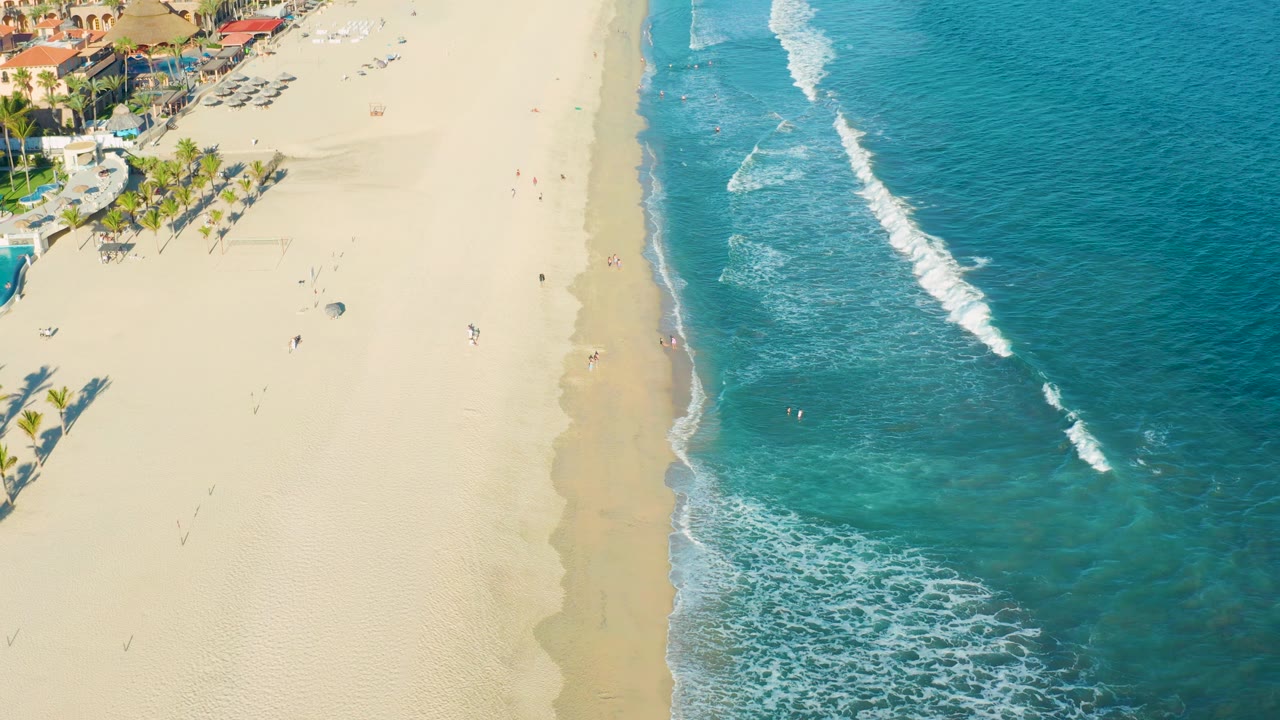 High aerial coastline view with surf breaking beside a wide sandy beach.
