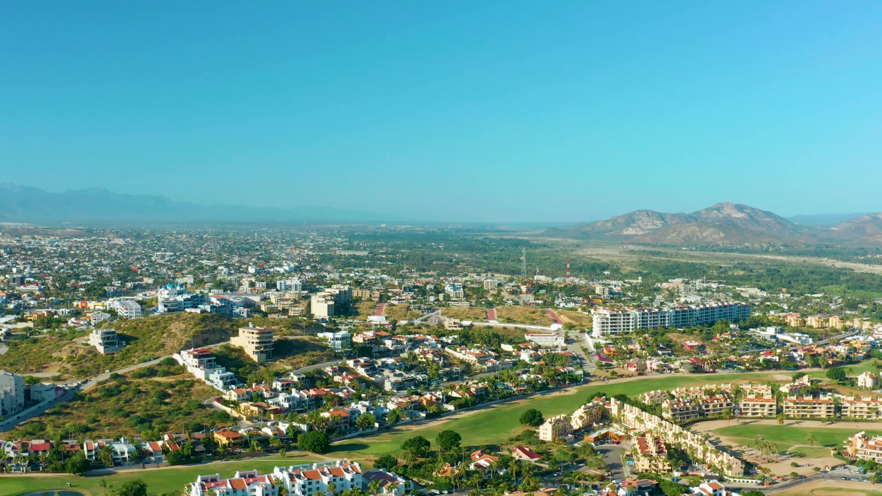 Residential aerial with a curving green area and mountains under clear sky.