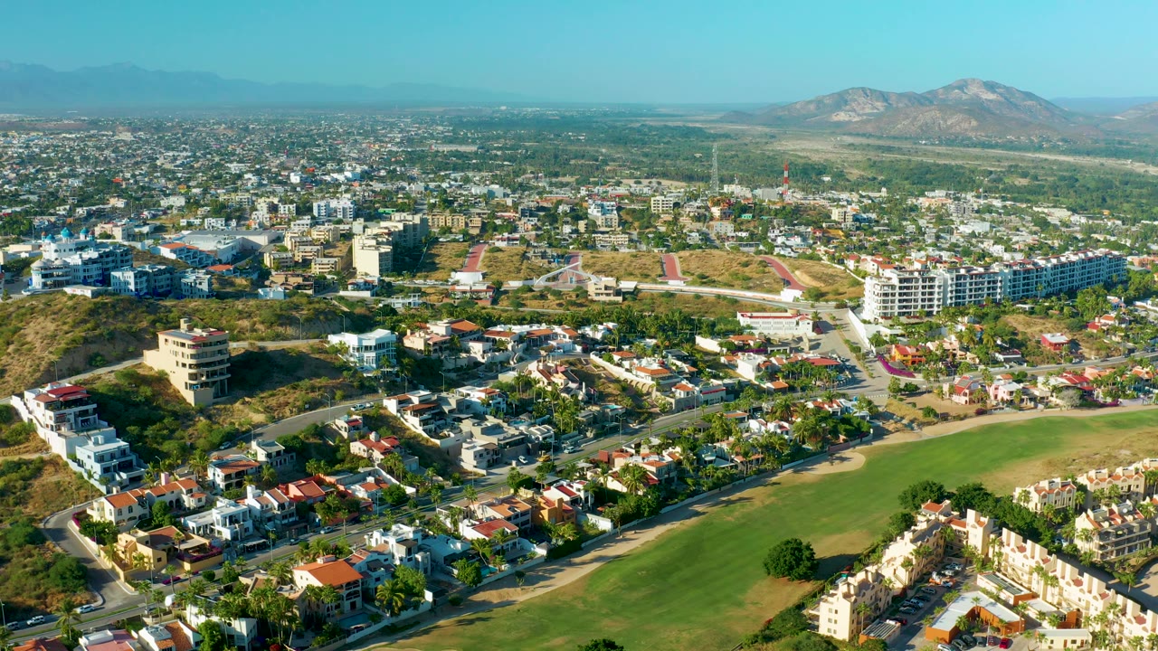 Wide drone-like view of a residential district, green space, hills, and mountains.
