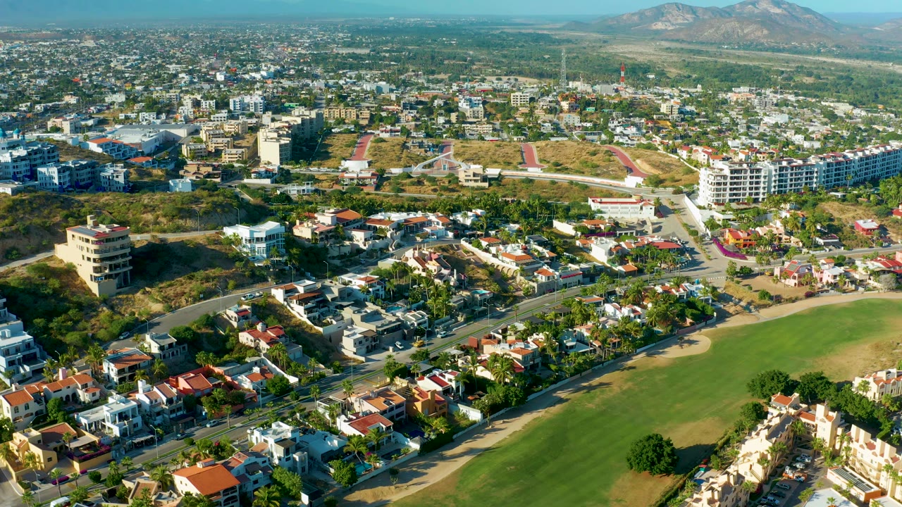 Aerial neighborhood view with homes, roads, field, and distant mountains.