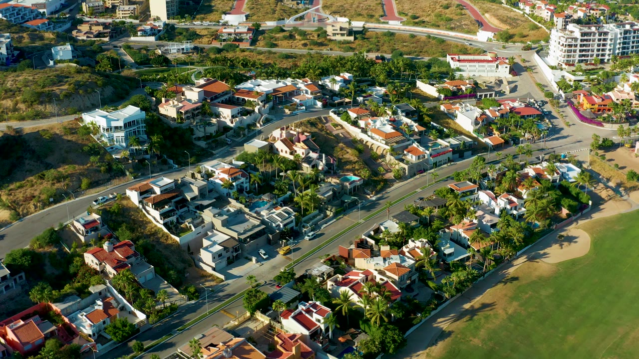 Aerial frame with homes, a main road, palms, and grassy land.