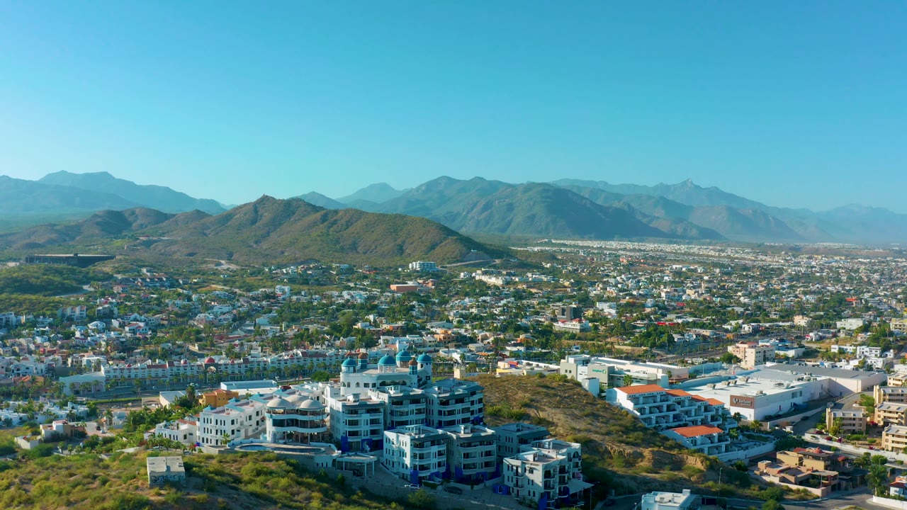 Hillside foreground with city and mountains under clear sky